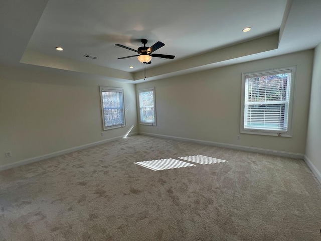 carpeted spare room with ceiling fan and a raised ceiling