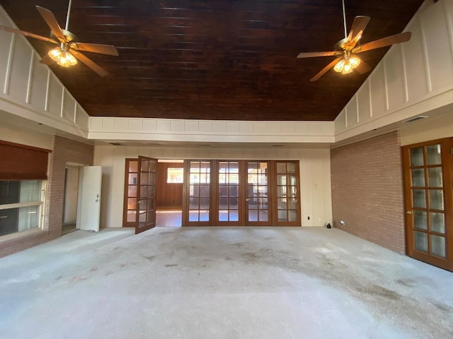 unfurnished living room featuring ceiling fan, french doors, high vaulted ceiling, and light colored carpet