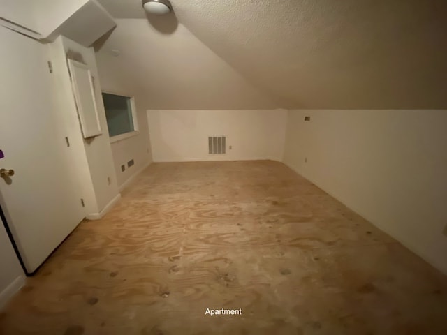 additional living space with a textured ceiling, light colored carpet, and vaulted ceiling