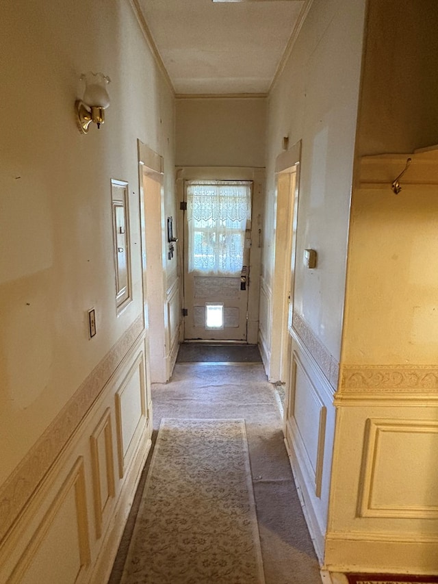 hallway featuring crown molding, a decorative wall, and a wainscoted wall