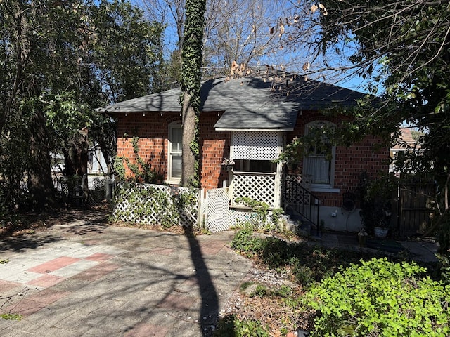 view of front of house featuring fence, a shingled roof, and brick siding