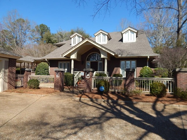 view of front facade featuring a fenced front yard, brick siding, roof with shingles, covered porch, and a gate