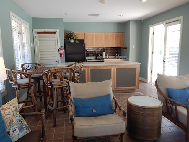 kitchen with light brown cabinets, light countertops, backsplash, freestanding refrigerator, and plenty of natural light