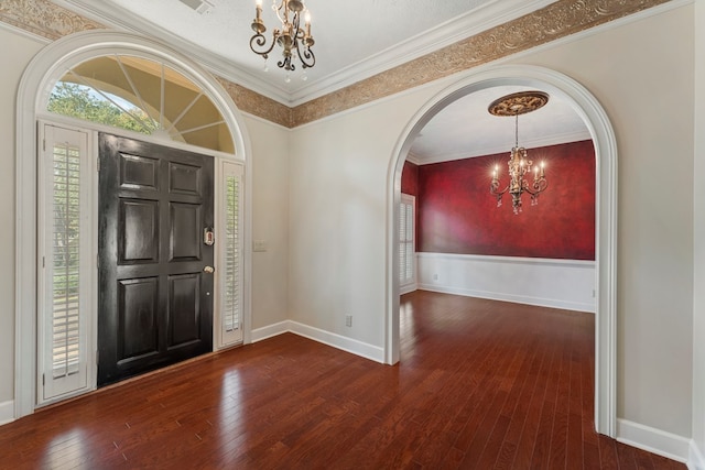 foyer entrance with arched walkways, hardwood / wood-style flooring, a notable chandelier, baseboards, and ornamental molding