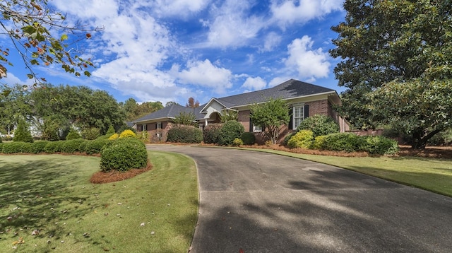 view of front of house with a front yard, brick siding, and driveway