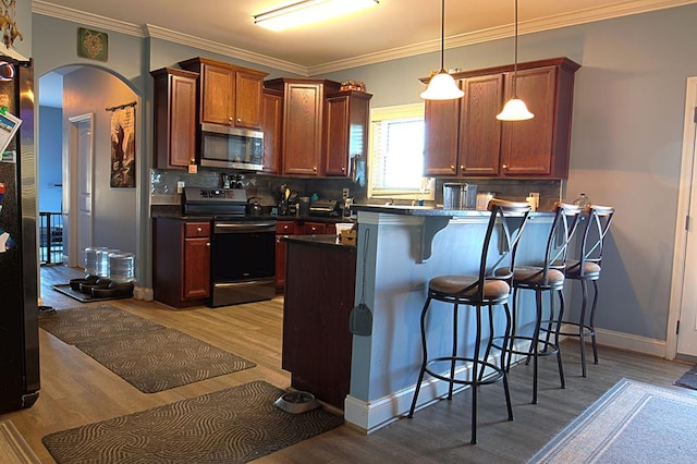 kitchen with appliances with stainless steel finishes, hanging light fixtures, backsplash, light hardwood / wood-style floors, and a kitchen bar