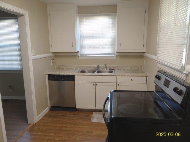 kitchen featuring stainless steel appliances, light countertops, white cabinetry, a sink, and wood finished floors