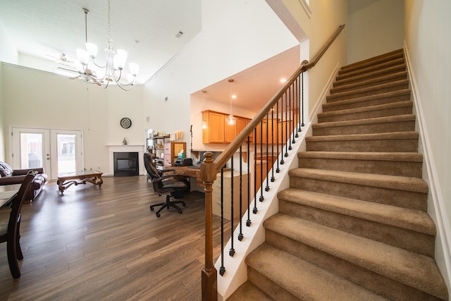 staircase featuring french doors, a towering ceiling, wood-type flooring, and a notable chandelier