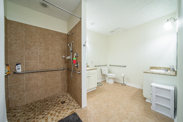 bathroom with toilet, a tile shower, and vanity