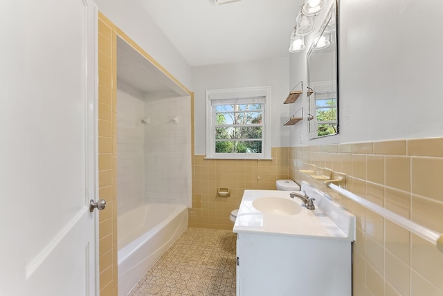 full bathroom with tile walls, toilet, vanity, and tiled shower / bath