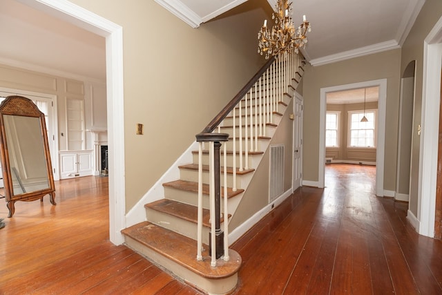 stairway with wood-type flooring, ornamental molding, visible vents, and an inviting chandelier