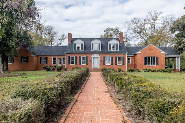 cape cod-style house with brick siding, a chimney, and a front yard