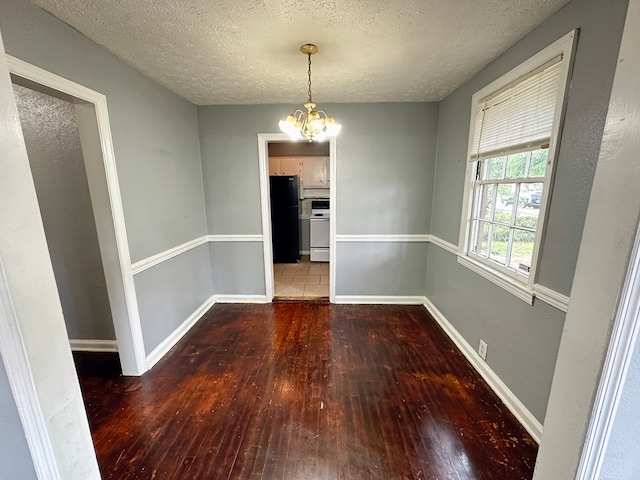 unfurnished dining area with dark hardwood / wood-style flooring, a textured ceiling, and a chandelier