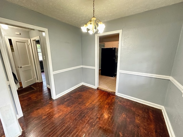 unfurnished dining area with a textured ceiling, dark hardwood / wood-style floors, and an inviting chandelier