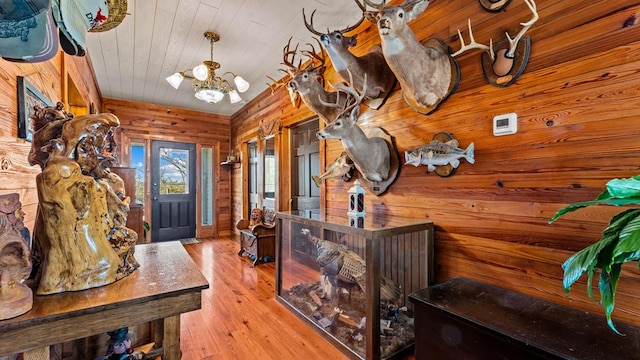 entrance foyer with an inviting chandelier, wood walls, wood ceiling, and light wood-type flooring