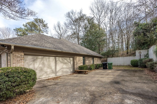 view of side of home with brick siding, a shingled roof, fence, and aphalt driveway