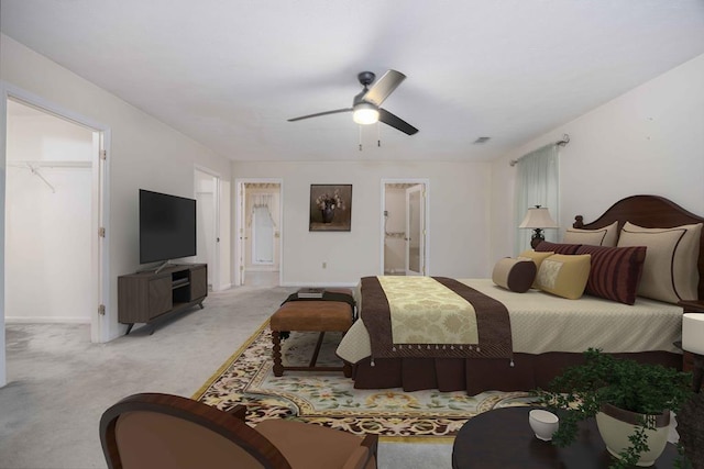 bedroom with baseboards, light colored carpet, ensuite bath, ceiling fan, and a walk in closet