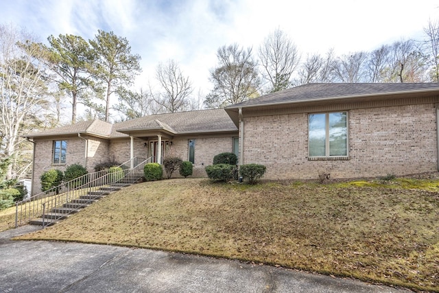 view of front of home with a shingled roof, a front lawn, and brick siding