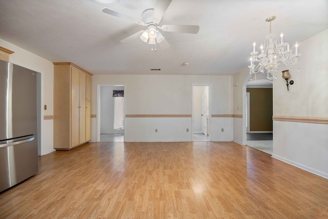 unfurnished living room with light wood-style floors, baseboards, arched walkways, and ceiling fan with notable chandelier