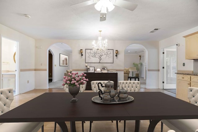 dining area featuring arched walkways, a textured ceiling, ceiling fan with notable chandelier, and visible vents