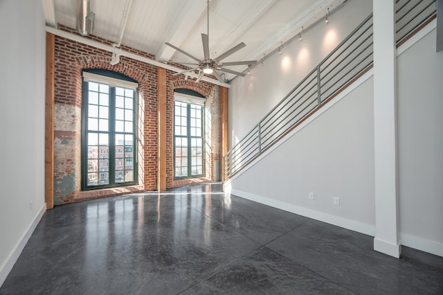 interior space with brick wall, ceiling fan, baseboards, stairway, and a towering ceiling