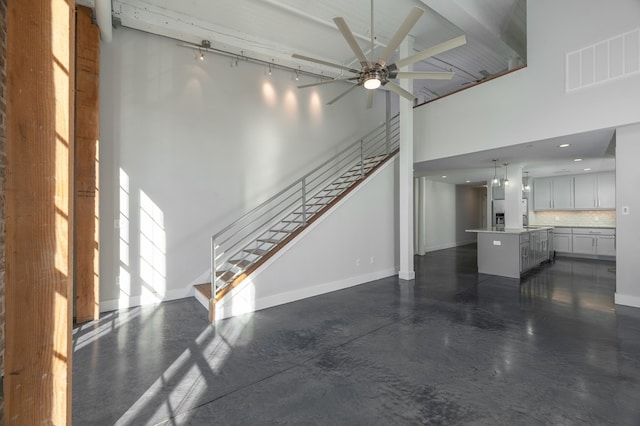 unfurnished living room featuring visible vents, a ceiling fan, stairway, a high ceiling, and baseboards