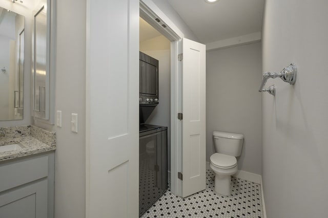 bathroom with vanity, toilet, baseboards, and stacked washing maching and dryer