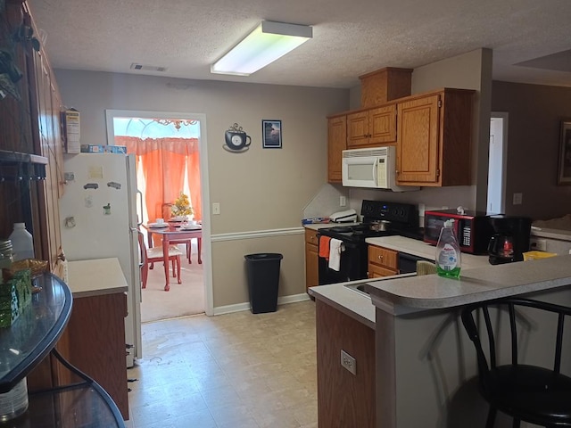 kitchen featuring white appliances, a breakfast bar area, kitchen peninsula, and a textured ceiling