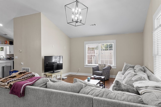 living area featuring wood finished floors, vaulted ceiling, visible vents, and a chandelier