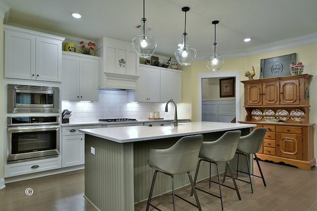 kitchen featuring white cabinets, decorative light fixtures, a center island with sink, and stainless steel appliances