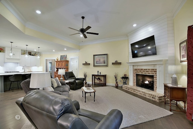 living room featuring a brick fireplace, ceiling fan, dark wood-type flooring, and ornamental molding