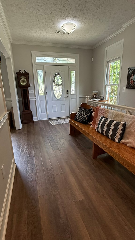 entryway featuring crown molding, a textured ceiling, dark wood finished floors, and visible vents