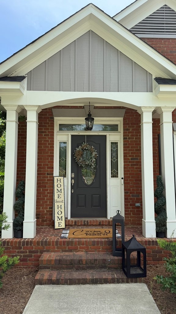 doorway to property featuring a porch, board and batten siding, and brick siding