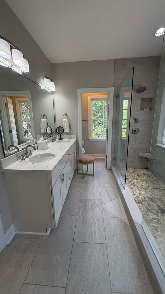 bathroom with a sink, a walk in shower, baseboards, and double vanity