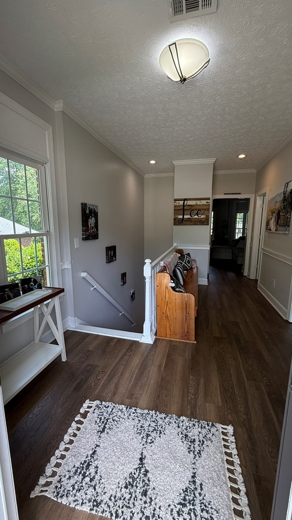 corridor with an upstairs landing, a healthy amount of sunlight, wood finished floors, and visible vents