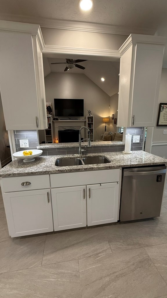 kitchen with light stone counters, a sink, dishwasher, open floor plan, and ornamental molding
