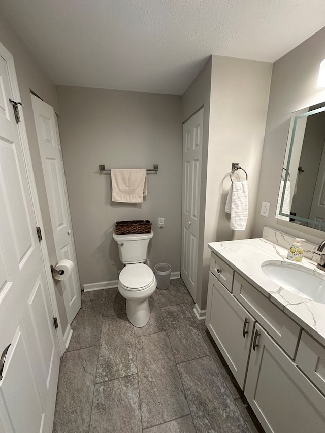 bathroom with baseboards, vanity, toilet, and a textured ceiling