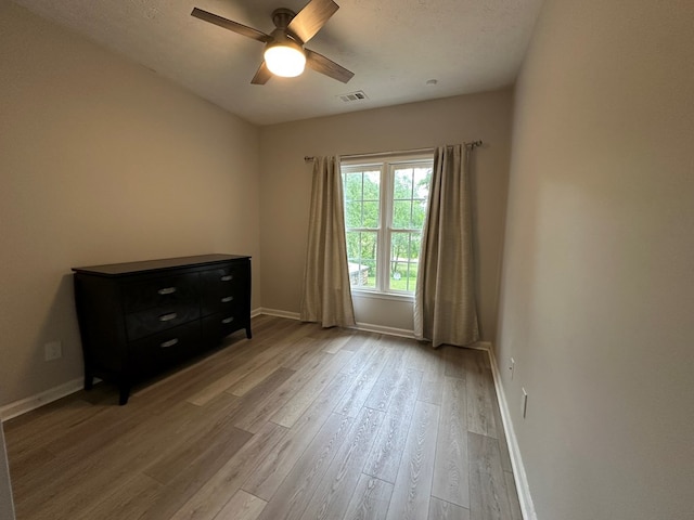 spare room featuring visible vents, light wood-style floors, baseboards, a textured ceiling, and a ceiling fan