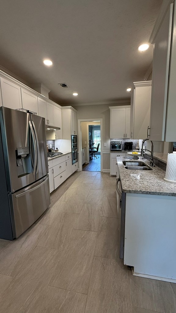 kitchen with visible vents, white cabinets, light stone counters, a sink, and stainless steel appliances
