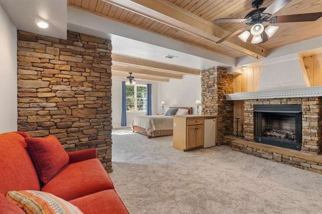 carpeted living room with ceiling fan, beam ceiling, a stone fireplace, and wood ceiling