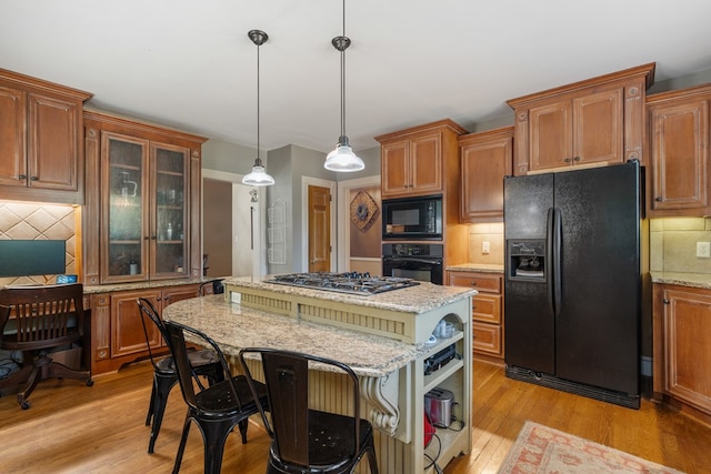 kitchen featuring a center island, backsplash, black appliances, light wood-type flooring, and decorative light fixtures