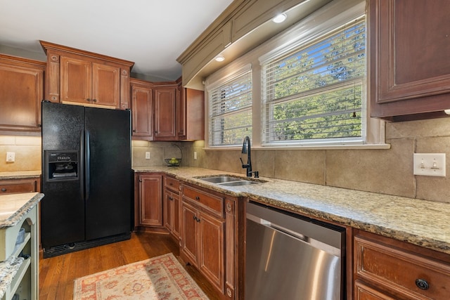 kitchen featuring tasteful backsplash, black refrigerator with ice dispenser, stainless steel dishwasher, sink, and hardwood / wood-style floors