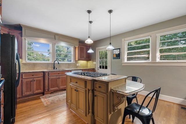 kitchen with stainless steel gas stovetop, a center island, black fridge, hanging light fixtures, and decorative backsplash