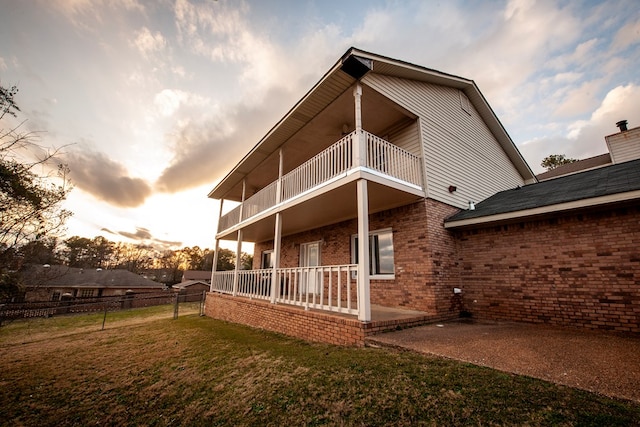 back of house with a lawn, a balcony, fence, a patio area, and brick siding