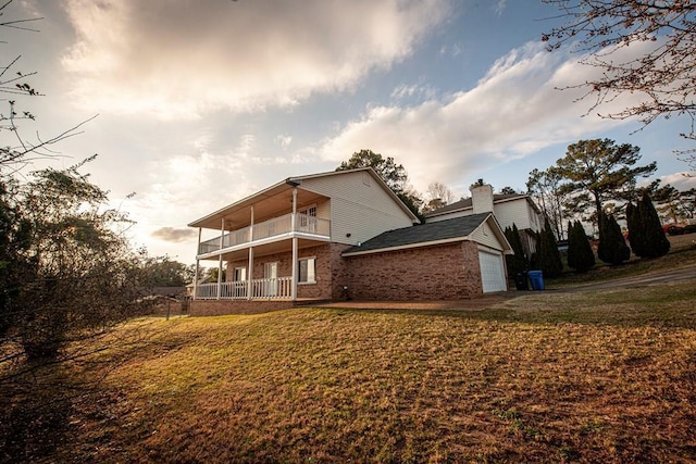 back of house featuring brick siding, a chimney, a lawn, a balcony, and a garage