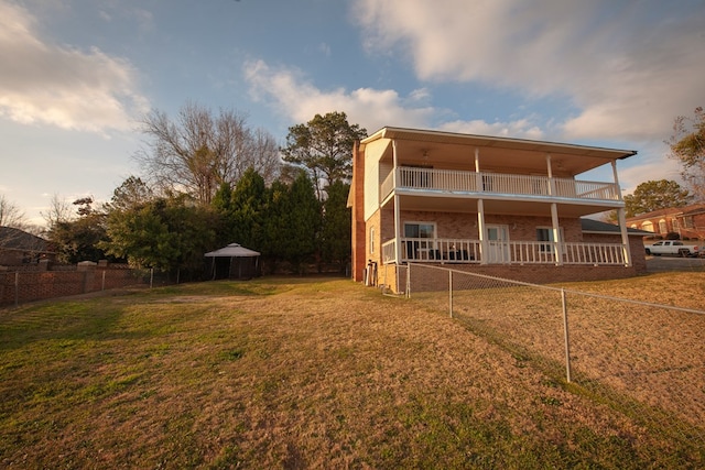 rear view of house with a balcony, brick siding, fence, a yard, and a gazebo