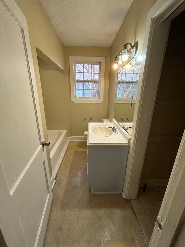 bathroom featuring vanity, a tub to relax in, toilet, and a textured ceiling