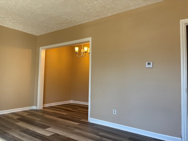 spare room featuring a textured ceiling, an inviting chandelier, and dark wood-type flooring