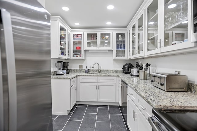 kitchen with light stone countertops, stainless steel appliances, white cabinetry, and sink