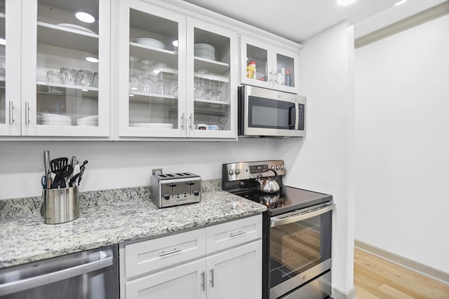 kitchen with light stone counters, white cabinets, stainless steel appliances, and light hardwood / wood-style floors